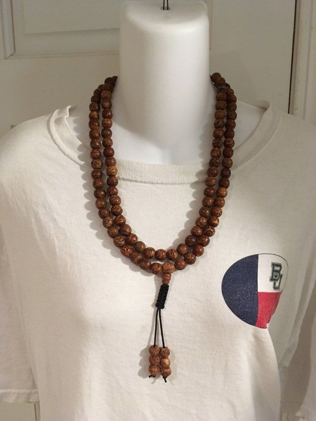 "Bodhi seed mala necklace made of 108 12mm beads with a Bodhi seed guru bead and an adjustable knot that allows you to change the length and tightness of the beads. Bodhi seeds are usually not polished so they are a solid color with small ridges or veins. Bodhi in Sanskrit translates to \"enlightened\" or \"awakened,\" therefore the Bodhi seed means \"enlightened seed.\" Bodhi is also a term in Buddhism to reflect a Buddha's understanding of the true nature of things. Many Buddhist wear the Bodh Spiritual Rosary With Round Beads For Meditation, Spiritual Rosary For Meditation With Round Beads, Spiritual Rosary With Large Beads, Holistic Wooden Beads Mala For Festivals, Adjustable Mala With 108 Beads For Rituals, Traditional Wooden Beads Necklace For Meditation, Adjustable Spiritual Hand-strung Mala, Adjustable Brown Mala For Healing, Traditional Wooden Bead Necklaces For Meditation