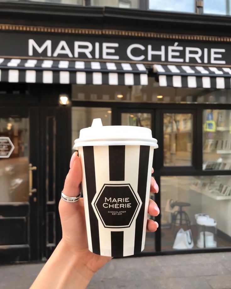 a person holding up a cup of coffee in front of a building with black and white stripes