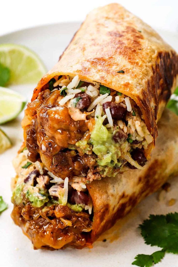 a burrito cut in half on a plate with cilantro and limes