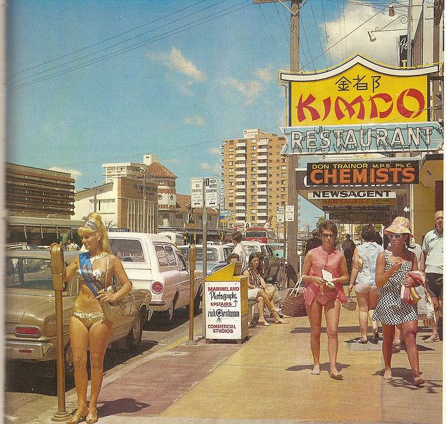 several women in bathing suits are walking down the sidewalk near cars and buildings on a sunny day