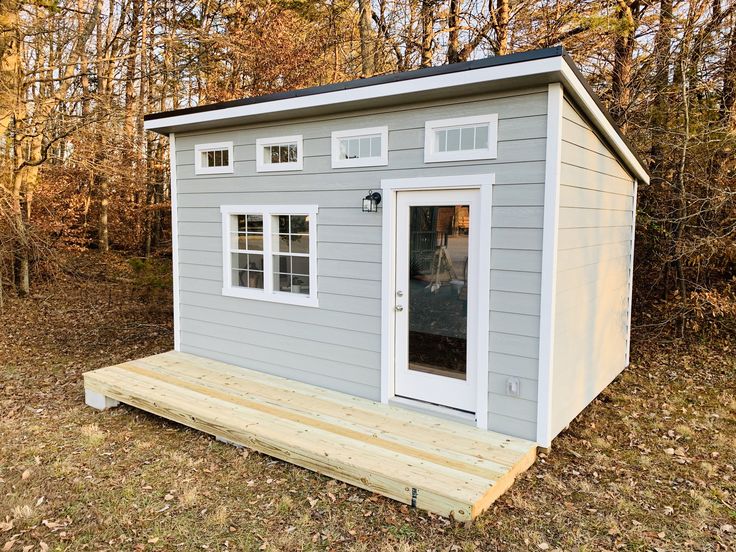 a small gray shed sitting on top of a wooden platform in front of some trees