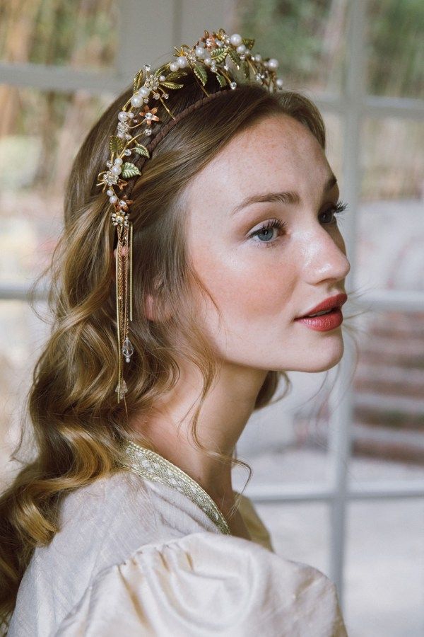 a woman with long hair wearing a gold head piece and pearls on it's side