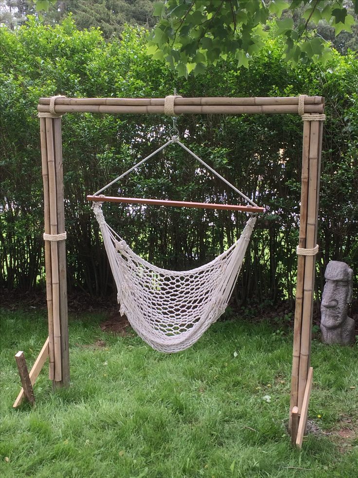 a white hammock hanging from a wooden frame in the grass next to a stone statue