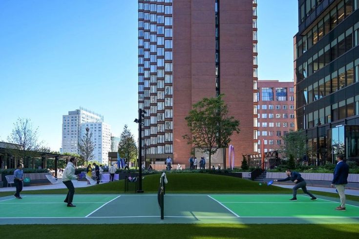 people are playing tennis on an artificial court in front of tall buildings and skyscrapers