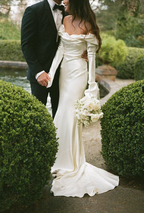 a bride and groom are standing in front of some bushes with their arms around each other