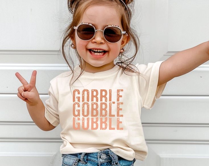 Celebrate Thanksgiving in style with our adorable Gobble Gobble t-shirt for girls! This festive and fun shirt is perfect for your little one to wear on Turkey Day, whether she's helping in the kitchen, enjoying the family feast, or participating in Thanksgiving activities. With a cute turkey and playful "Gobble Gobble" text, your little turkey will be the center of attention! Product Details: Design: "Gobble Gobble" in playful, trendy lettering Material: Soft, breathable cotton blend for a comfortable all-day fit Sizes: Available in toddler, baby and youth sizes. Fit: Classic fit, perfect for layering with cardigans or jackets Care Instructions: Machine wash cold, tumble dry low Why You'll Love It: -Adorable Thanksgiving-themed design with fun "Gobble Gobble" text -Soft and cozy fabric per Funny Toddler Thanksgiving Shirt, Diy Thanksgiving Shirts For Kids, Thanksgiving Shirts For Kids, Kids Thanksgiving Shirts, Trendy Lettering, Toddler Thanksgiving Shirt, Kids Shirts Design, Cute Turkey, Funny Thanksgiving Shirts