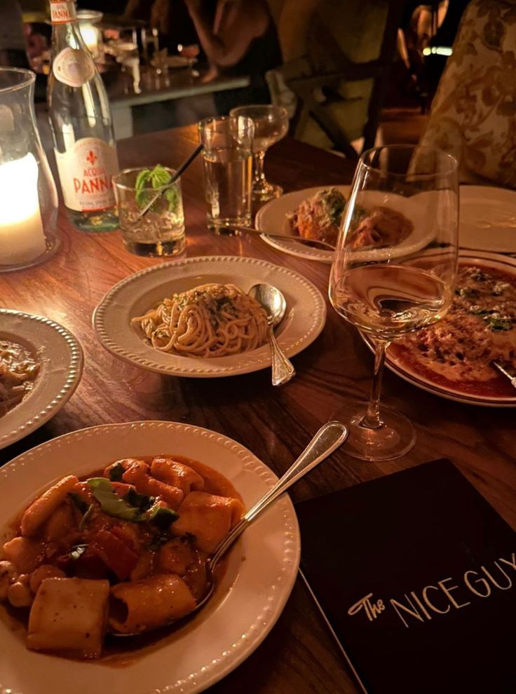 a wooden table topped with plates of food and glasses filled with wine next to candles