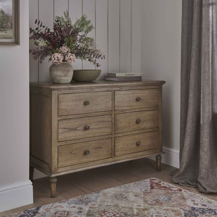 a wooden dresser sitting next to a window filled with flowers and greenery on top of it