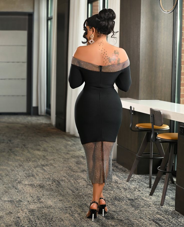 a woman in a black dress is walking down the hallway with her hand on her hip