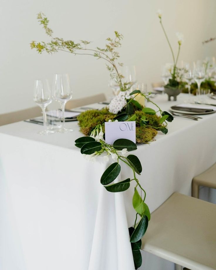 the table is set with white linens, greenery and place cards for guests