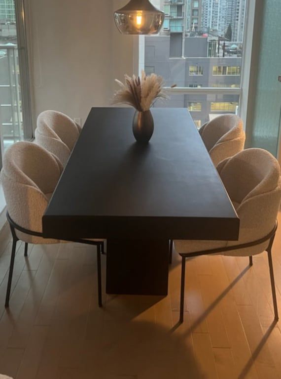 a dining room table with chairs and a vase on top of it in front of a window