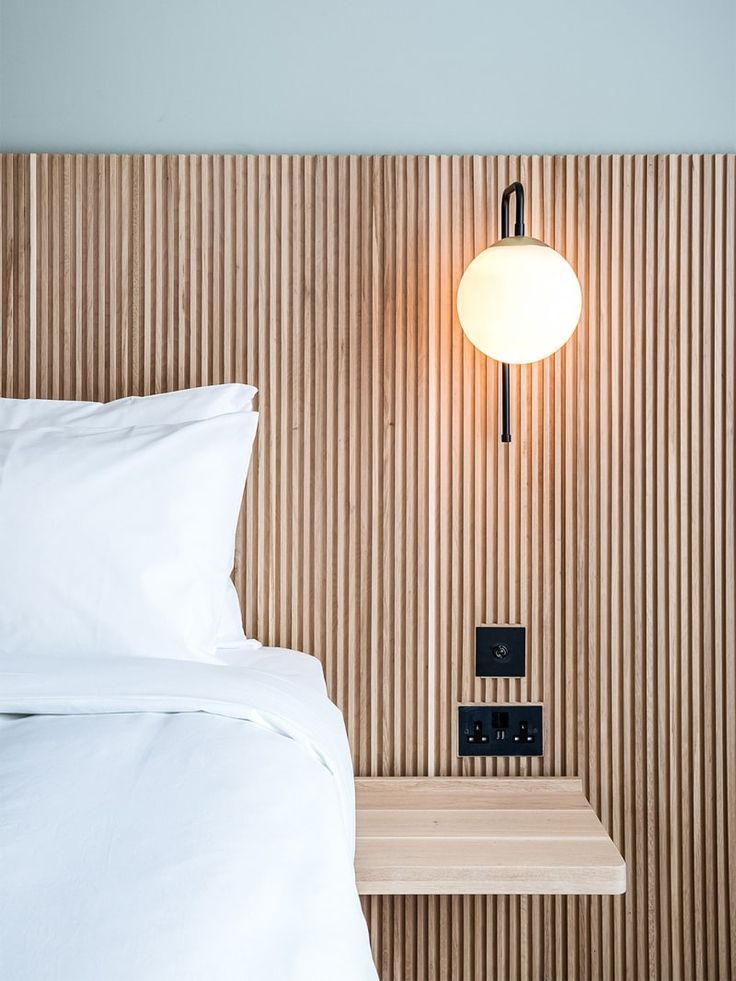 a white bed sitting next to a wooden headboard with a lamp on top of it