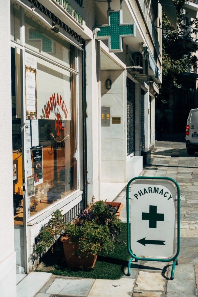 a pharmacy sign sitting on the side of a road next to a store front window