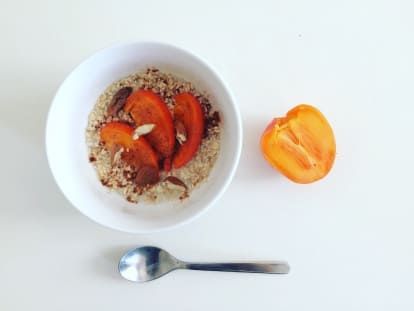 a white bowl filled with oatmeal and fruit next to a spoon