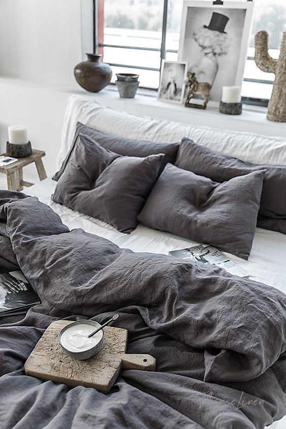 an unmade bed with grey linens and pillows