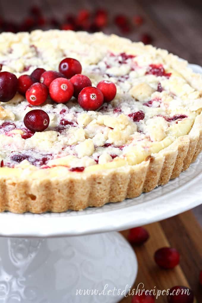 cranberry cheesecake on a cake plate with fresh cranberries scattered around it