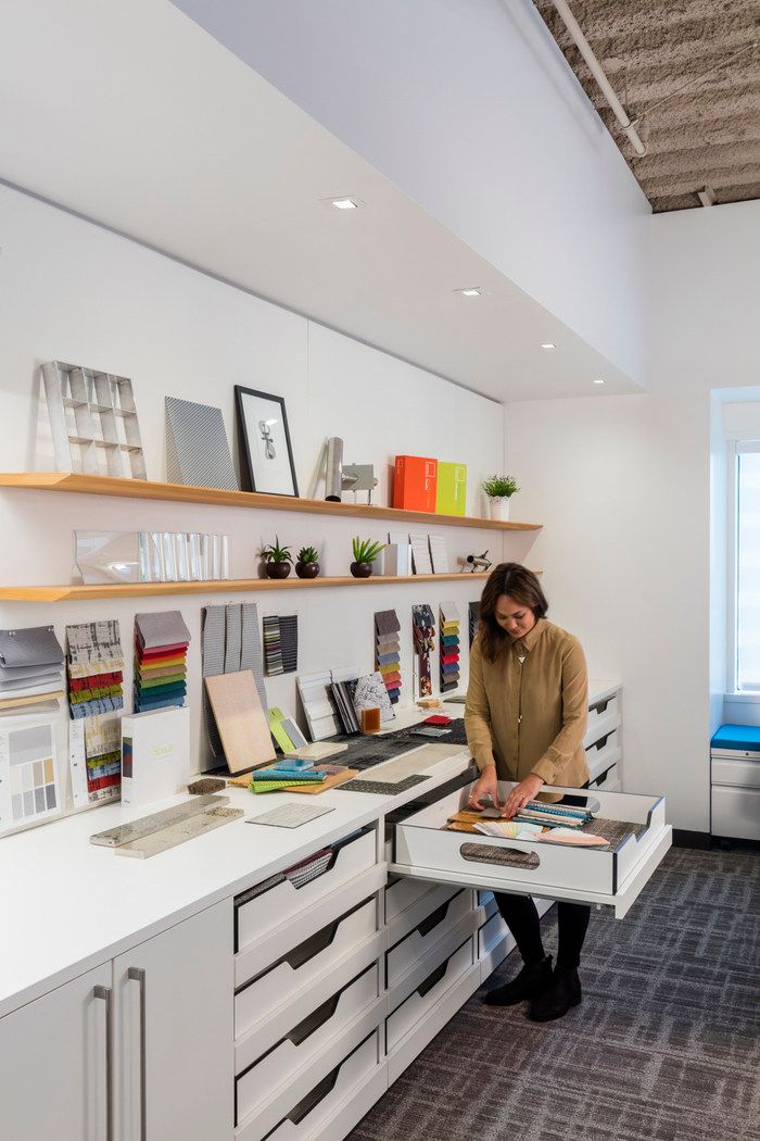 a woman sitting at a desk in an office with lots of papers on the shelves