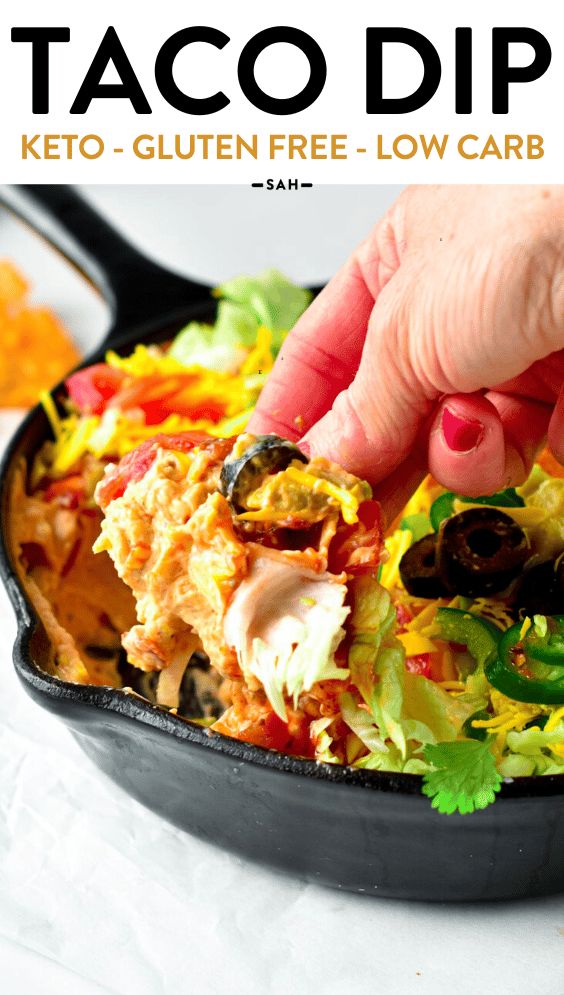 a person dipping sauce on top of a salad in a cast iron skillet with lettuce, tomatoes and black olives