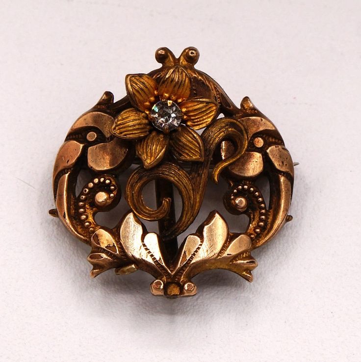 This vintage brooch pendant is a stunning piece of art nouveau jewelry that combines floral and fauna motifs in a unique and beautiful way. The main stone is a round glass gemstone with a width and length of 3.13 mm, and a white/colorless color that complements the yellow gold, gold plated silver base metal and brass.  It a great gift for occasions such as Mother's Day, Christmas, weddings, birthdays, and Valentine's Day.  The vintage piece has a metal purity of 10-12K and country of origin unkn Luxury Gold Art Nouveau Brooches, Luxury Collectible Art Nouveau Brooch, Luxury Art Nouveau Wedding Brooches, Floral And Fauna, Glass Range, Christmas Weddings, Nouveau Jewelry, Pendant Brooch, Art Nouveau Floral