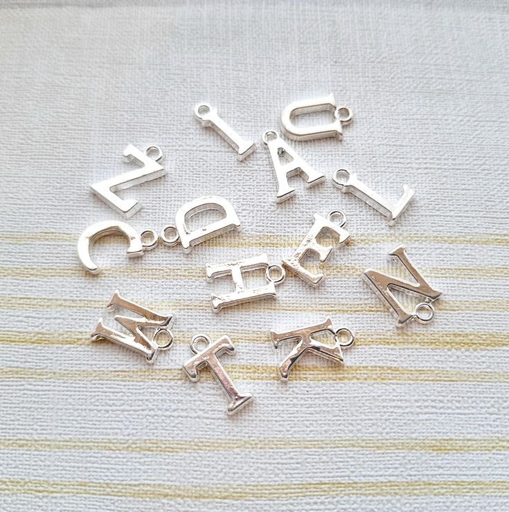 silver plated charms with letters and numbers on a white cloth background, one is for each letter