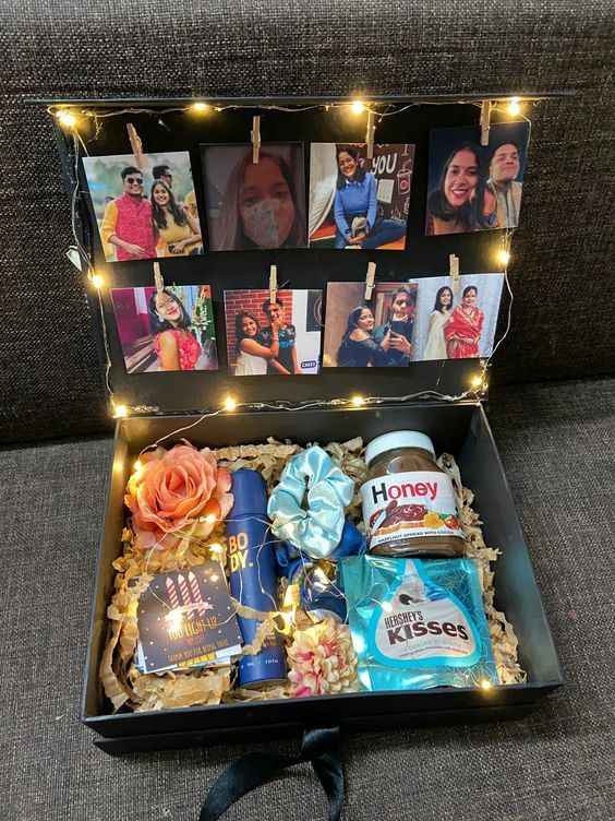 an open gift box filled with personalized items and pictures on clothes pins attached to string lights