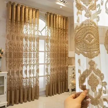 the curtains in this living room are decorated with gold and white laces, which is being held by someone's hand