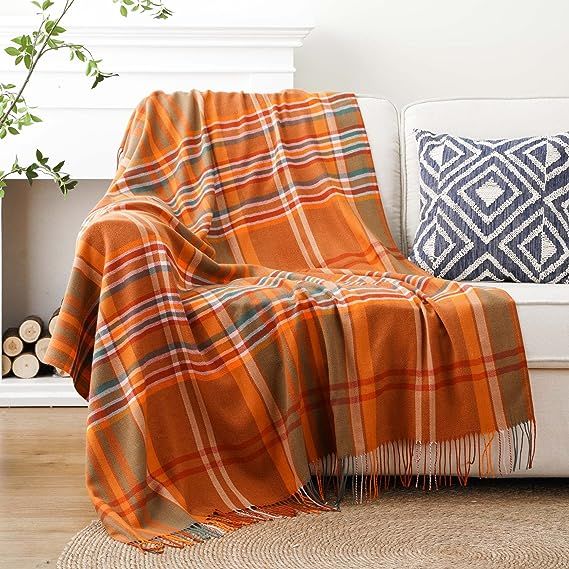 an orange plaid blanket sitting on top of a white couch next to a plant in a living room