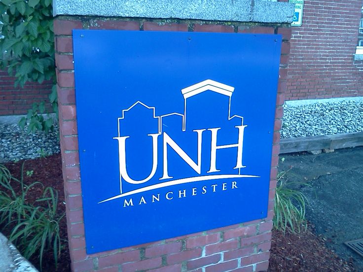 a blue sign that reads unh manchester in front of a brick wall and bushes