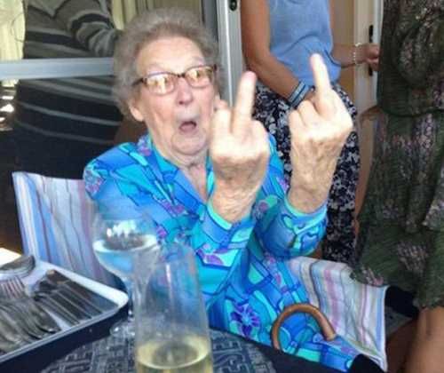 an older woman sitting at a table making the peace sign