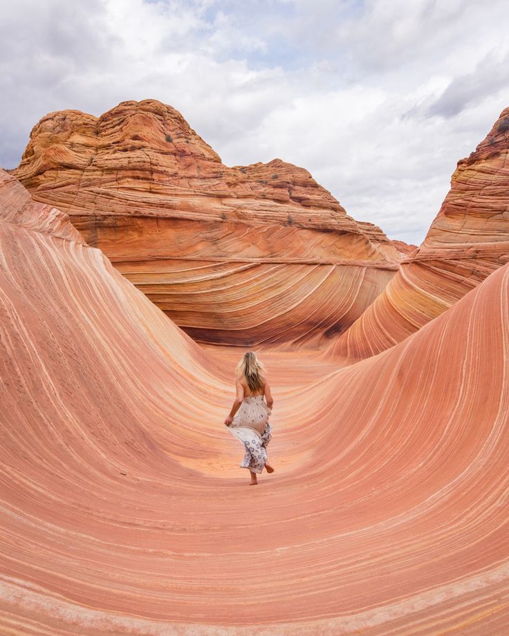 a woman standing in the middle of an area with red rock formations and sand dunes