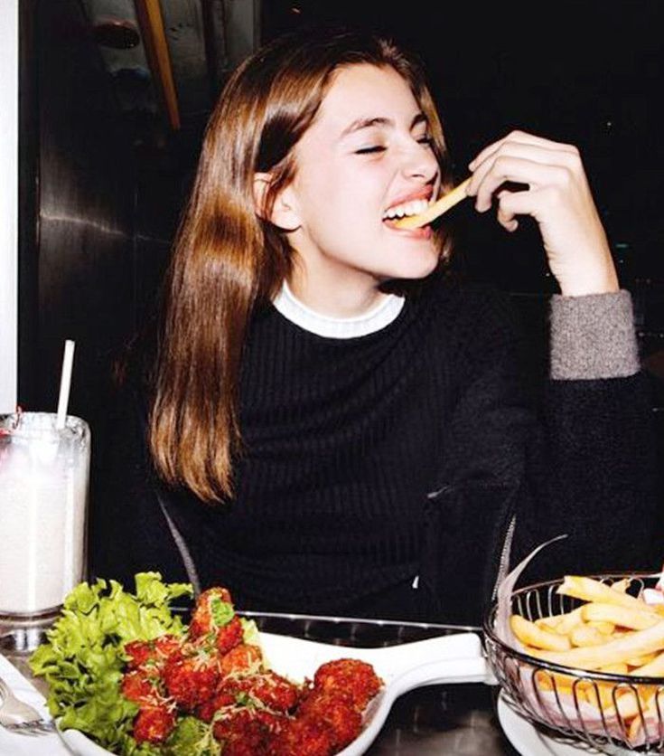 a woman sitting at a table eating french fries and salad with a glass of milk in front of her