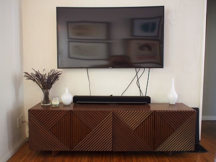 a flat screen tv mounted on the wall above a wooden cabinet with two vases