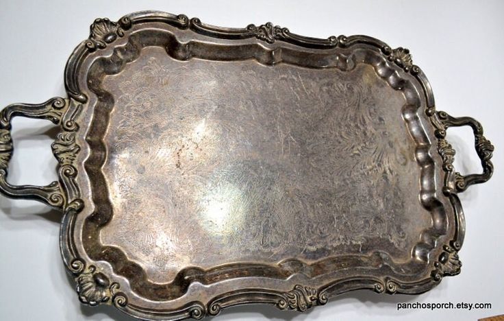 an ornate silver tray with handles on a white wall