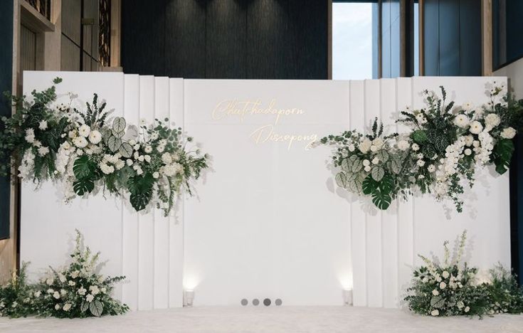 a white backdrop with flowers and greenery on the front is set up for a wedding ceremony