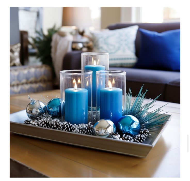 three blue candles sitting on top of a tray filled with christmas decorations and balls in front of a couch