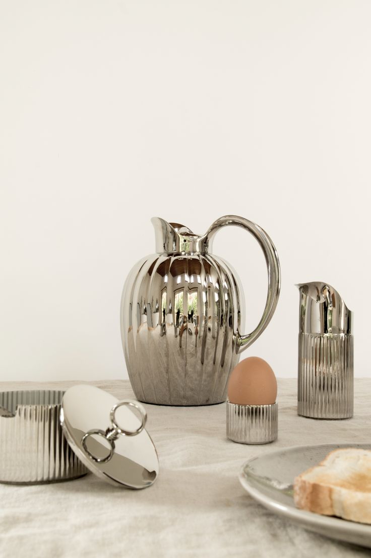 a table topped with silver dishes and utensils next to an egg on a plate