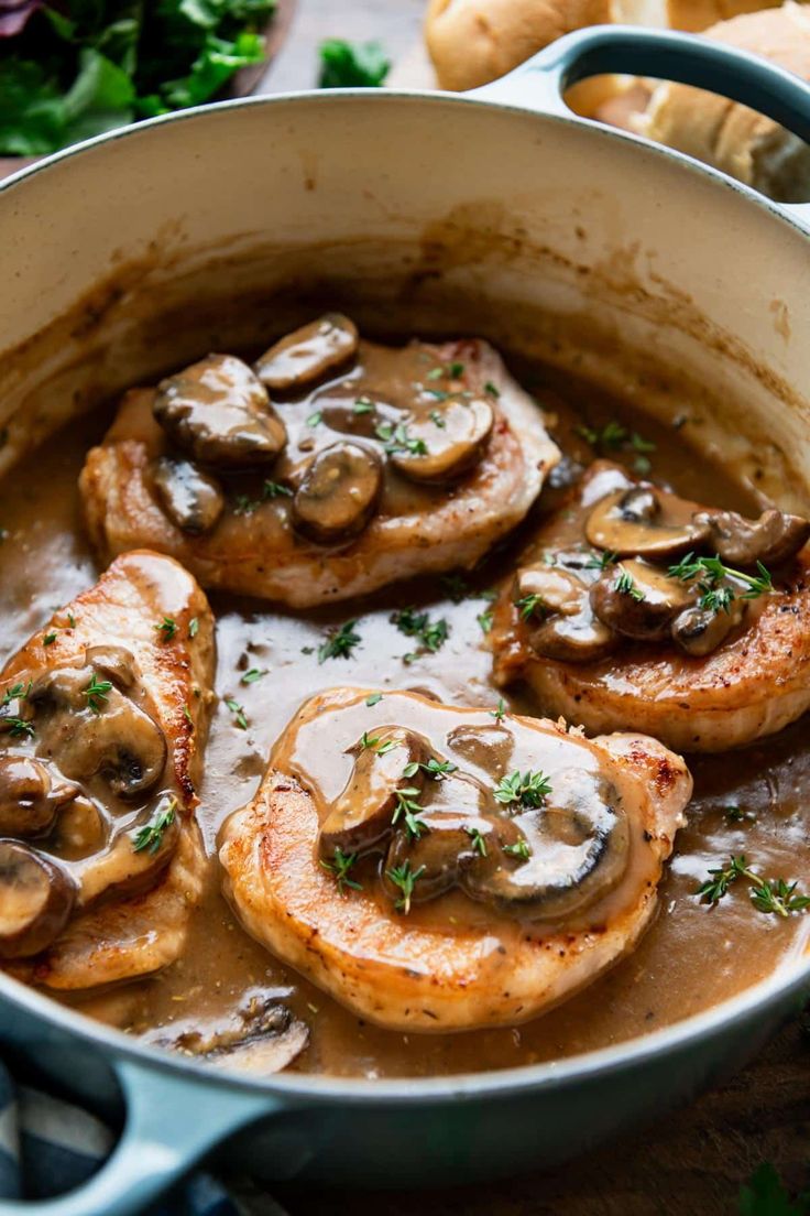 a pan filled with mushrooms and sauce on top of a wooden table next to bread