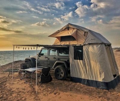 an suv is parked on the beach with a tent attached to it's roof