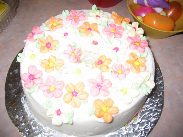 a cake with white frosting and colorful flowers on it sitting on top of a table