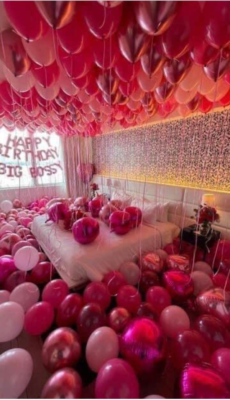 a room filled with lots of pink and white balloons floating in the air next to a bed