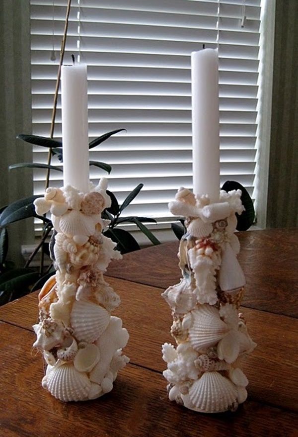 two candles with shells on them sitting on a table next to a plant and window