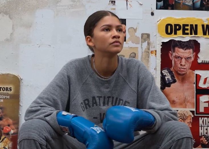 a woman sitting on the ground with boxing gloves in front of her and posters behind her