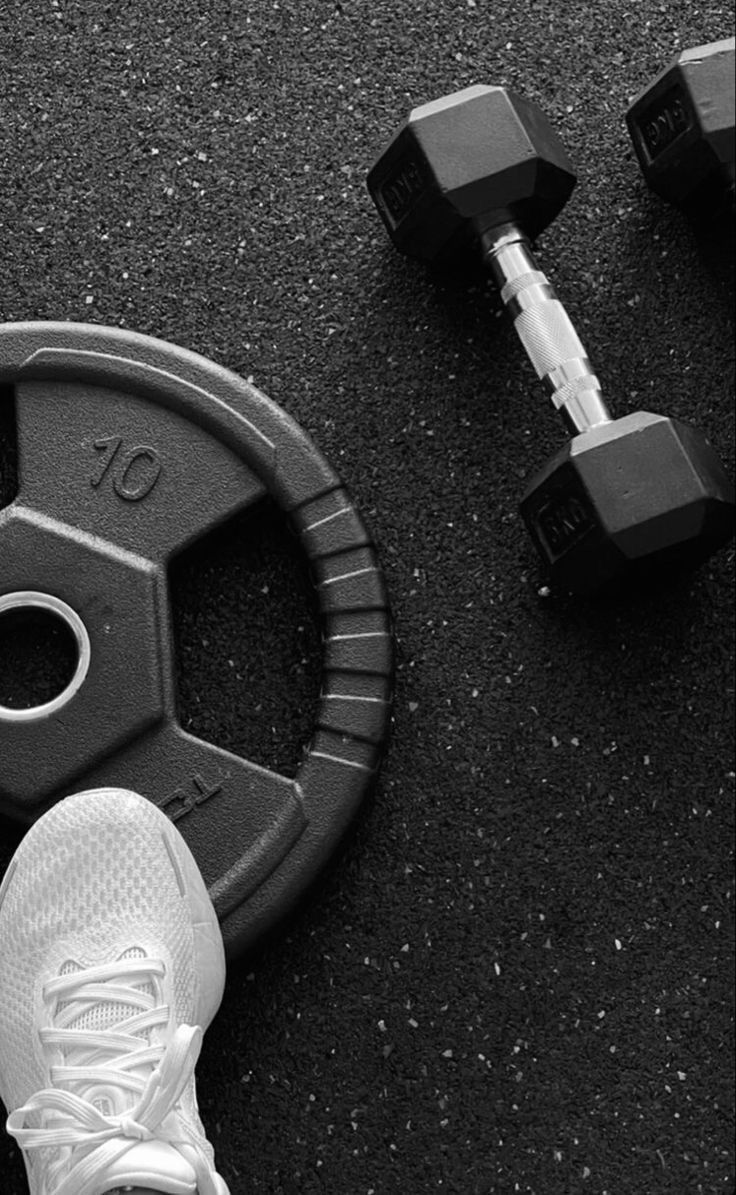 the feet of a person standing next to a pair of dumbbells