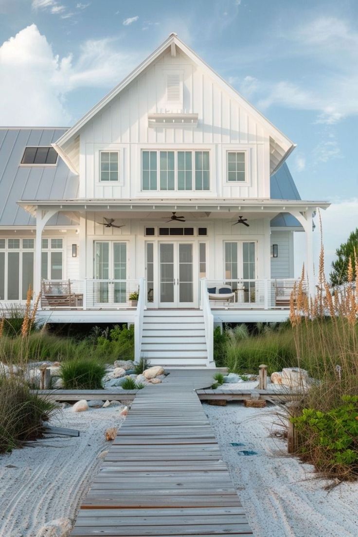 a large white house sitting on top of a sandy beach next to tall grass and plants