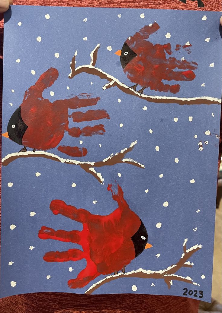 a child's handprint is shown with two red birds on a snowy branch