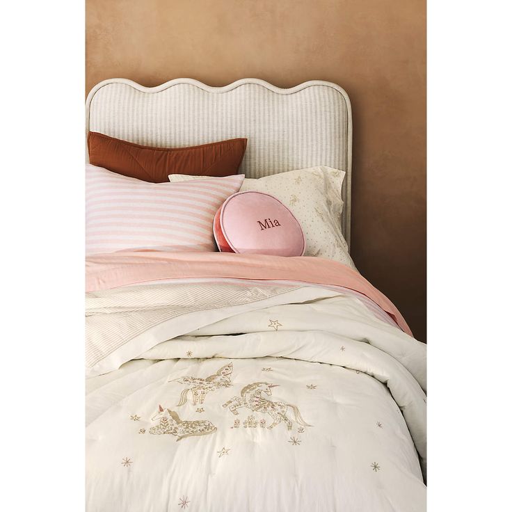 a white bed with pink and brown pillows on it's headboard next to a beige wall