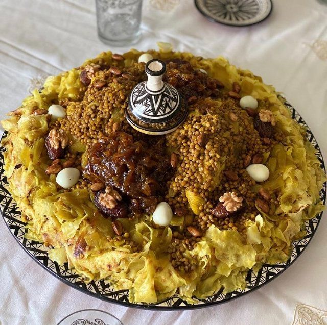 a cake with nuts and other toppings on a black plate sitting on a white table cloth