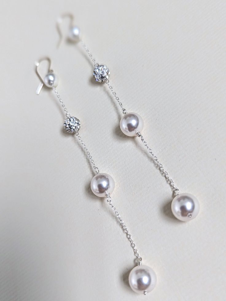 three pairs of pearl and diamond earrings on a white surface, with the pearls dangling from them