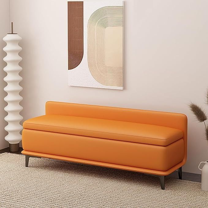 an orange couch sitting in front of a painting on the wall next to a vase