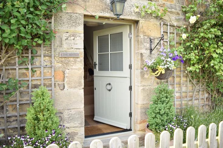 an open door to a stone building with flowers growing on the outside and in front